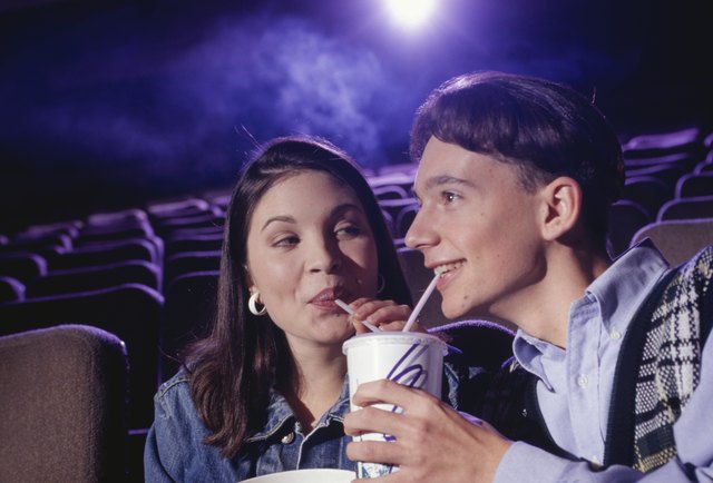 Teenage couple (16-17) sitting in cinema with popcorn, sharing soda