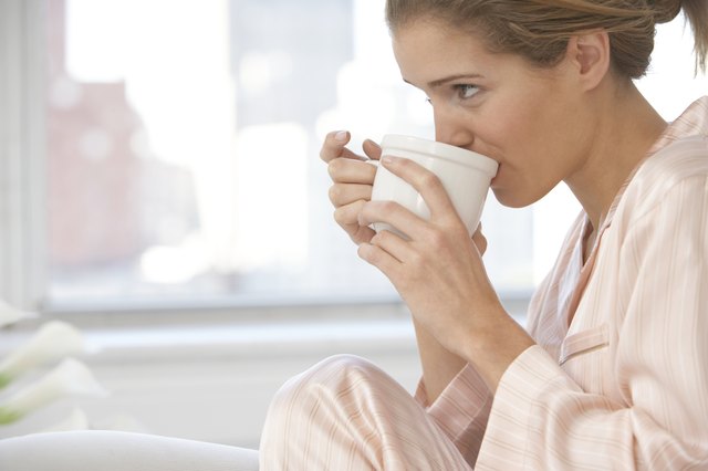 Young woman wearing pyjamas, drinking from cup, close-up