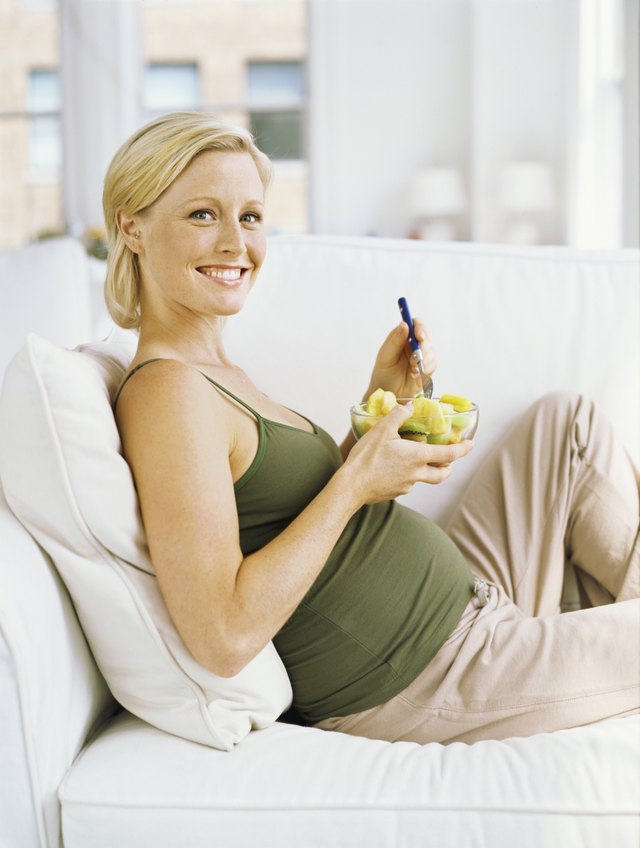 portrait of a pregnant woman smiling and holding a bowl of fruit salad