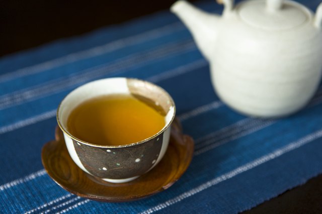 High Angle View of a Tea Cup Filled with Tea and a Tea Pot in the Background, Differential Focus, Close Up