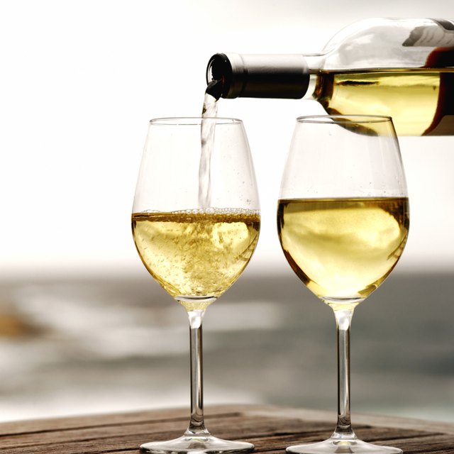 bottle of white wine being poured and two glasses