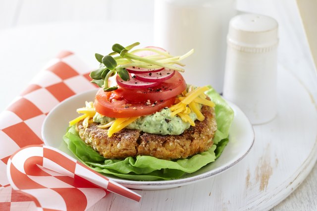 Gluten free chickpea burger with lettuce, guacamole, shredded cheddar cheese, tomatoes, red onion, and sprouts