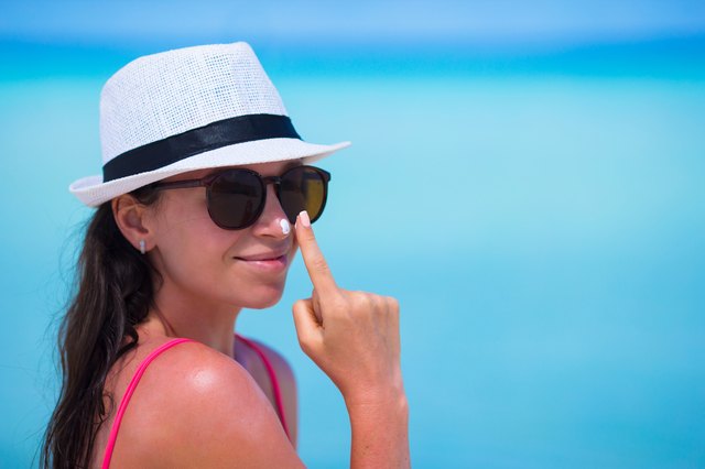 Young woman applying suntan lotion on her nose on beach