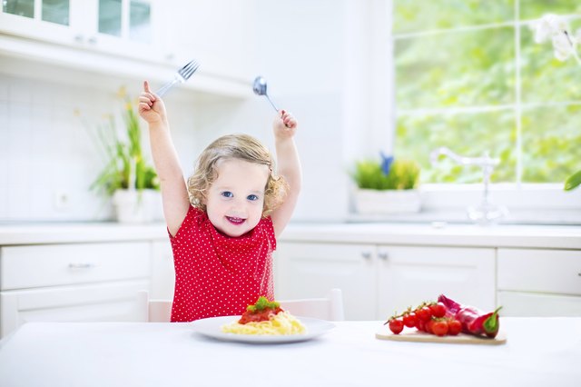 Cute toddler girl eating spaghetti in a white kitchen