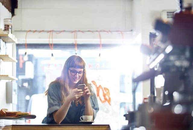Woman checks her mobile phone with forward neck tilt while drinking coffee.