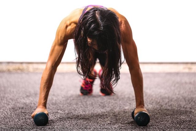 A fit woman work uses dumbbells to enhance her push-up.