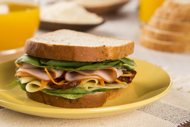 Sandwich on a white plate with turkey breast, tomato, lettuce.