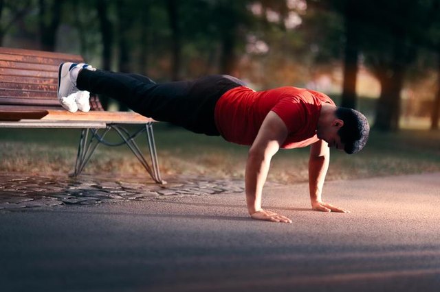 Athletic guy doing push-ups with his fit on a bench