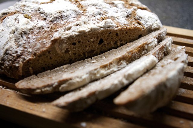 Loaf of sourdough bread partly sliced on a wooden board