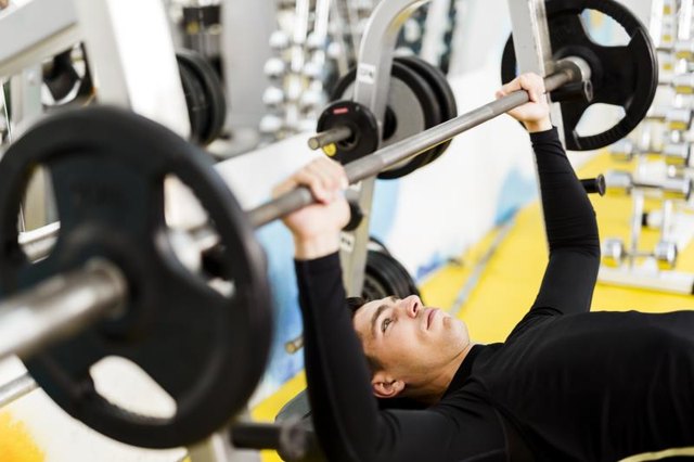 A young man prepares for a standard barbell bench press on a flat bench.