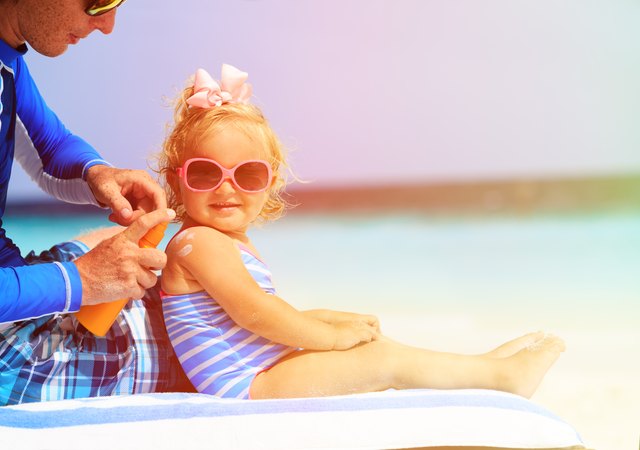 father applying sunblock cream on daughters shoulder