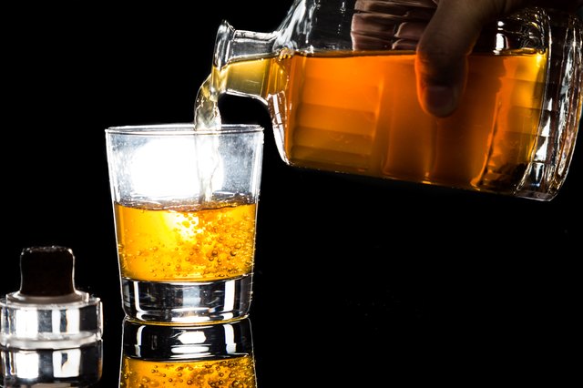 Hand pouring whiskey into glass against dark background