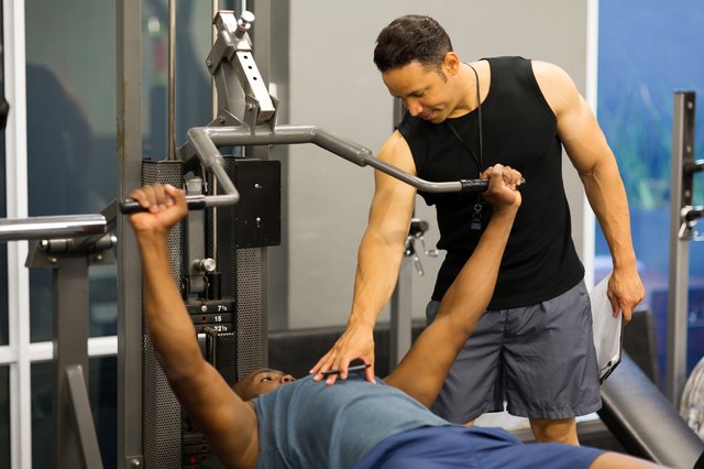 personal trainer helping client lift weights