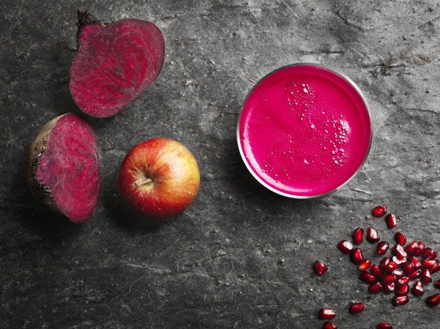 Overhead view of pink raw juice and red fruit and vegetables on dark background