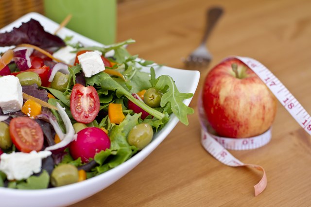 Healthy green salad and an apple with measuring tape