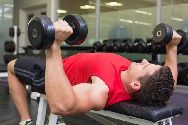 Bodybuilder lying on bench lifting dumbbells