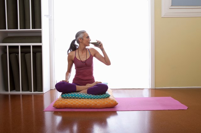 Woman sitting cross legged on cushion drinking water