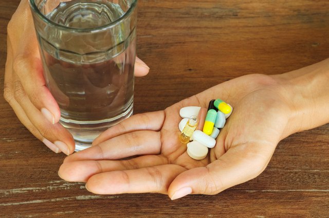 female hands holding pills, capsules, medicine,vitamin and water glass