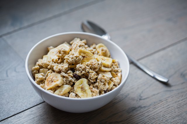 Bowl of granola with banana slices with milk on table.