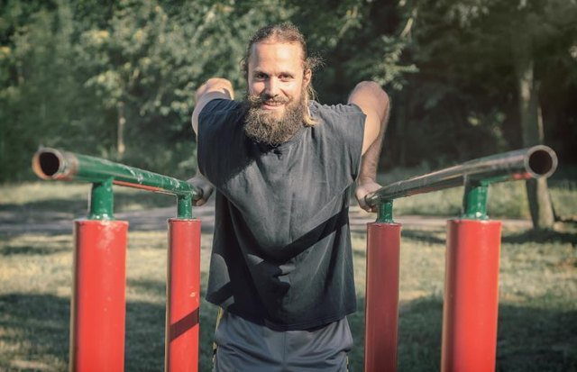 Training outdoors. Man doing biceps and triceps dips training on horizontal bars in the sport park.