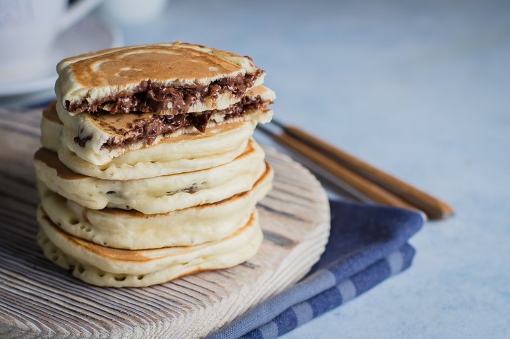 Stack of stuffed chocolate nutella pancakes on vintage wooden board on blue table background with cup of tea. American Breakfast Concept. Copy space