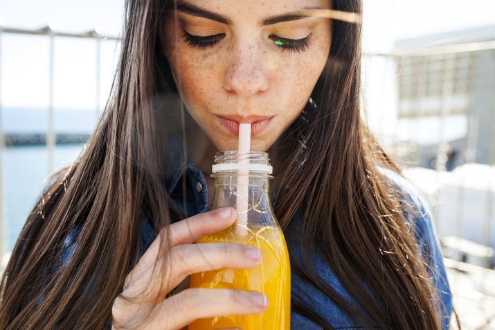 Young woman with freckles drinking orange juice