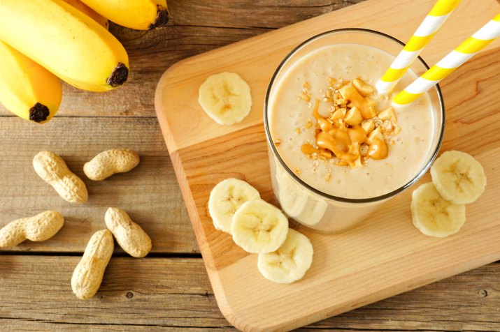 Peanut-butter banana oat smoothie with straws, on wood