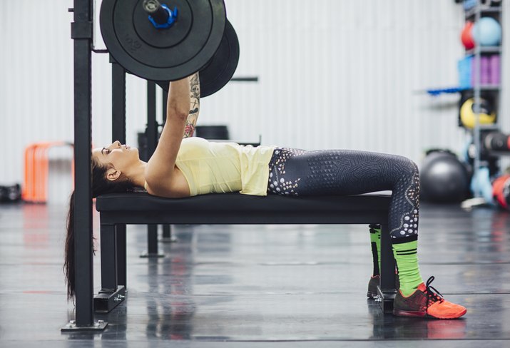 Woman lifting deadlift while lying on bench press in gym
