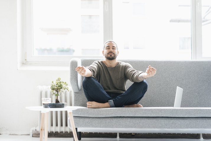 Portrait of man with eyes closed sitting on the couch doing yoga exercise