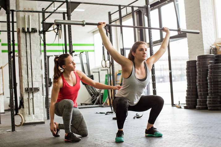 Personal trainer guiding woman doing barbell squats at gym
