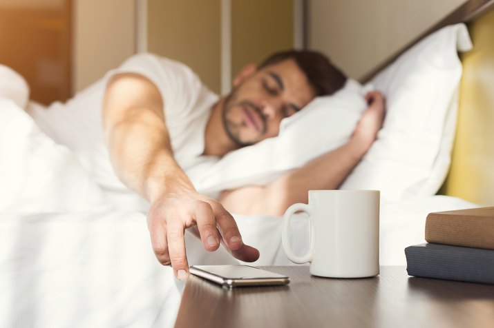 Sleepy guy waking up early after alarm clock signal