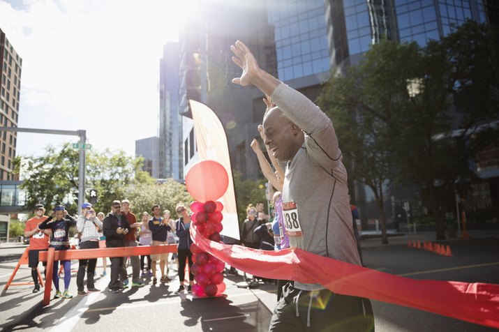 Exuberant male marathon runner crossing finish line with arms raised