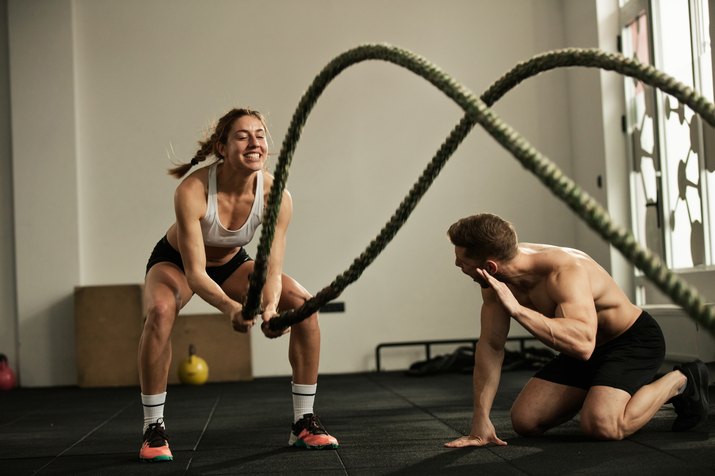 Athletic woman doing battle rope exercise with personal trainer in a gym.