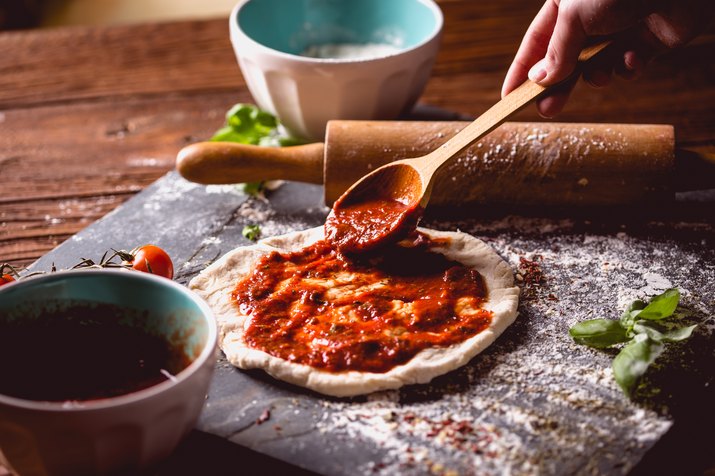 Girl is placing tomato sauce on fresh pizza