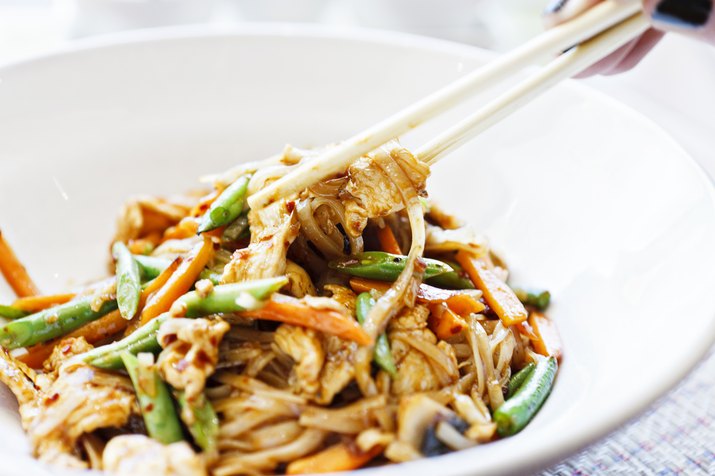 Woman's hand uses chopsticks to serve Thai chicken noodle dish