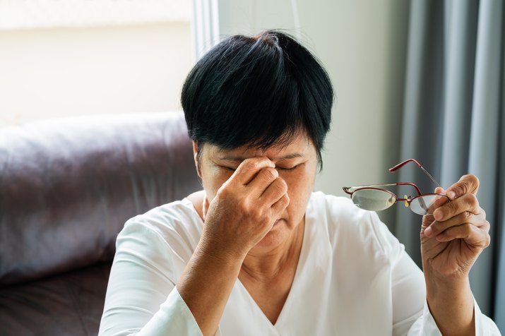 女子在读纸质书后摘下眼镜，按摩眼睛。因长时间戴眼镜而感到不适、头晕