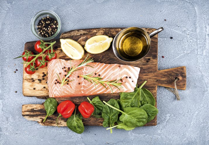 Ingredients for cooking healthy dinner. Raw salmon fillet, spinach, tomatoes, olive oil, lemon, peppers, rosemary and spices on a rustic wooden board
