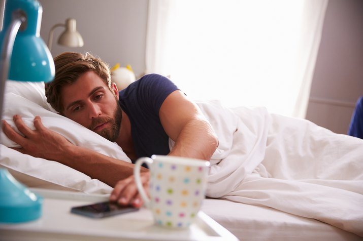 A man in bed woken up by his cell phone on nightstand