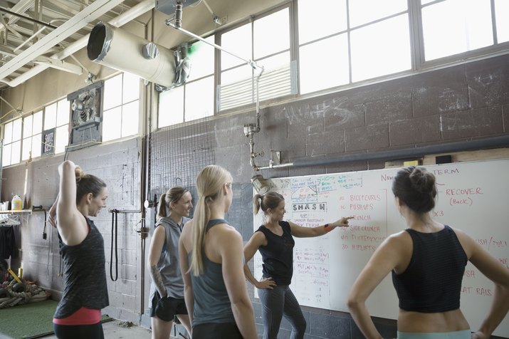 Female instructor and gym students at whiteboard in gritty gym