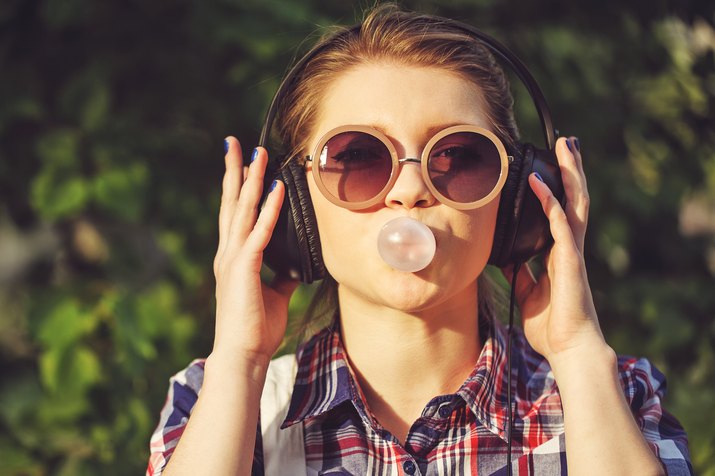 Hipster girl listening to music on headphones and chews cud.