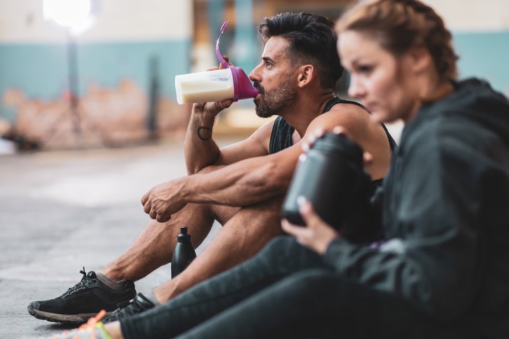 Man and woman in sports clothing drinking protein drinks