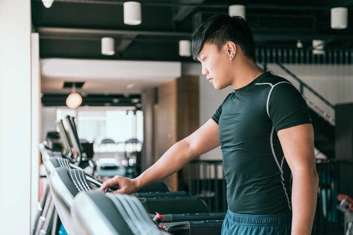 Male runner set up treadmill in gym