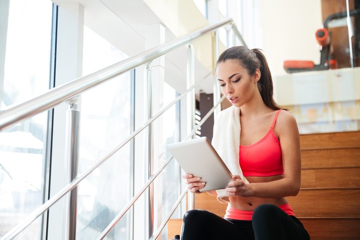 Thougtful sportswoman using tablet after training in gym