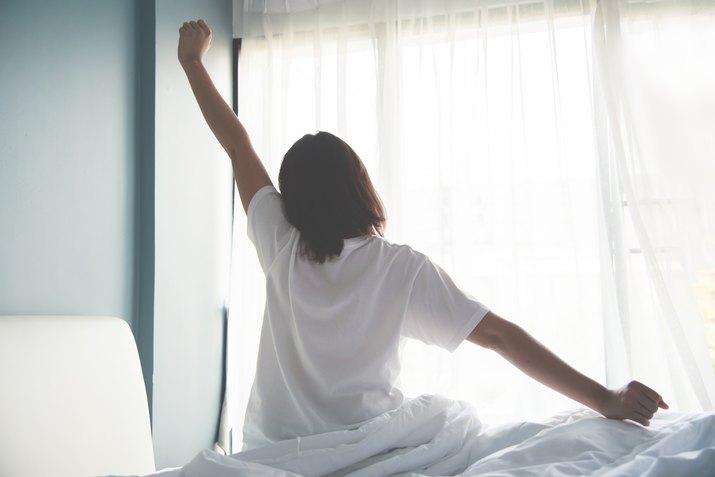 Asian woman waking up in the morning. Outstretched arms.