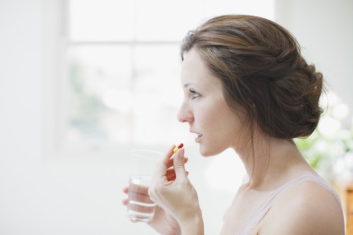 Woman holding glass of water and taking capsule