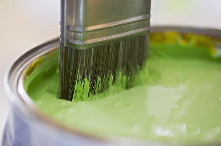 Paintbrush dipped in to a pot of green paint, close up
