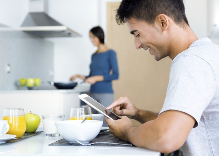 Couple in the kitchen preparing breakfast and browsing  internet