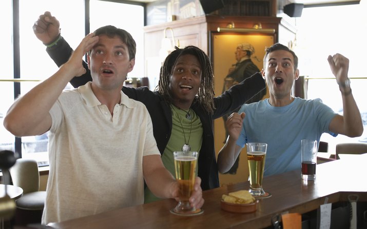 Three men drinking at bar, cheering and looking upwards