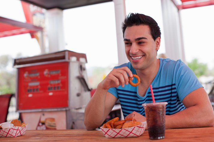 Young man eating onion rings in diner, smiling