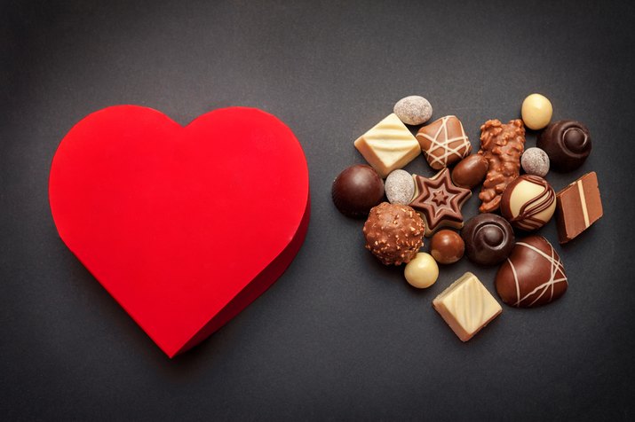 Red heart shaped box with chocolate pralines on dark background